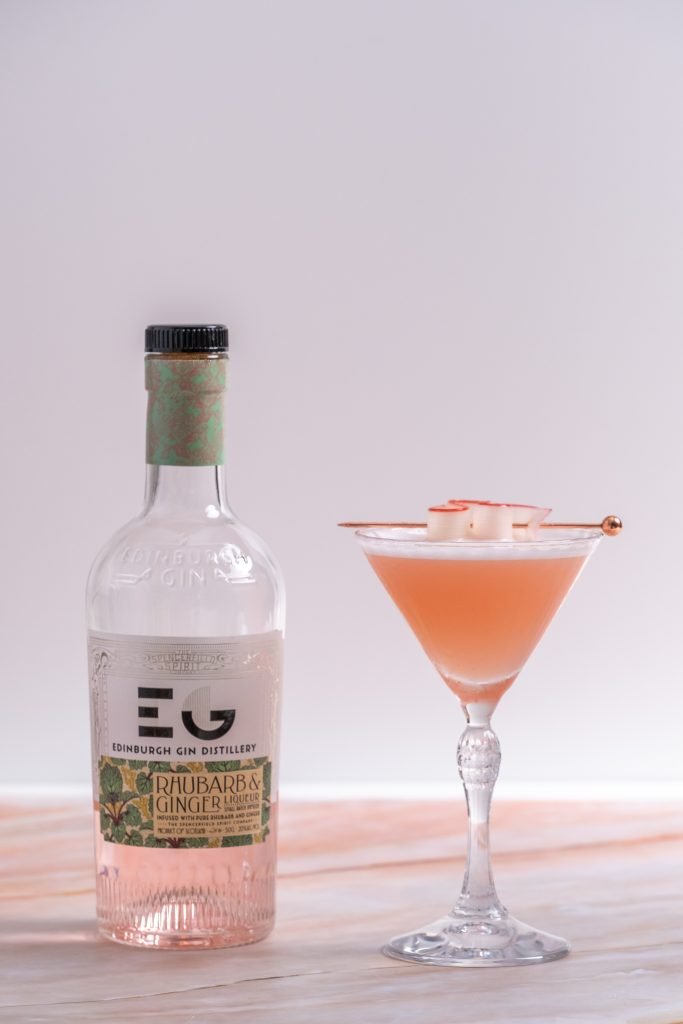 Vertical image front view, rhubarb ginger gin cocktail in martini glass with edinburgh distillery rhubarb ginger gin bottle.