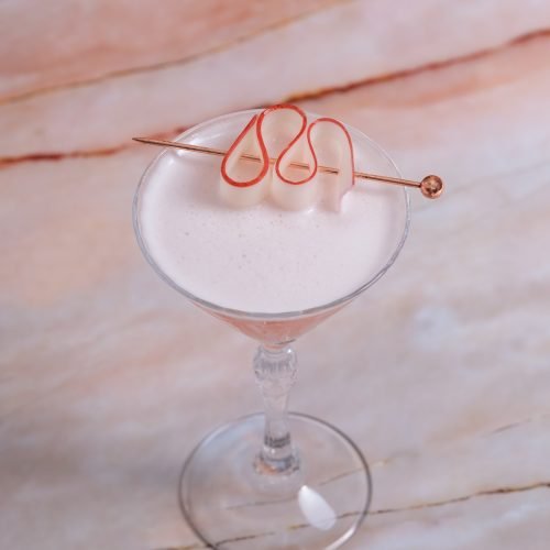 high angle view, vertical image of a rhubarb ginger gin cocktail in a martini glass, on a pink marble table.