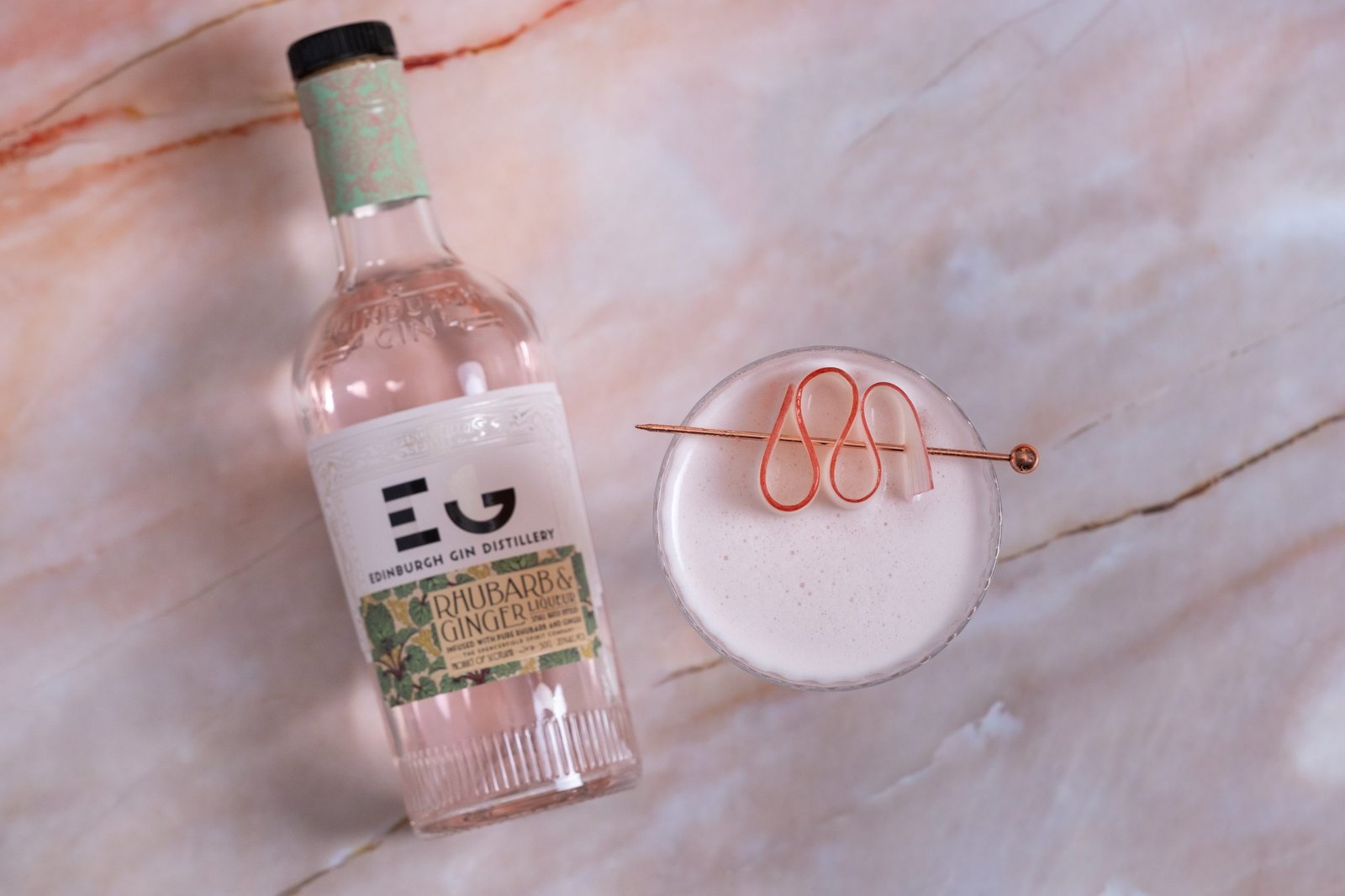 Top view of a rhubarb ginger gin cocktail with a bottle of edinburgh gin distillery's rhubarb ginger gin.